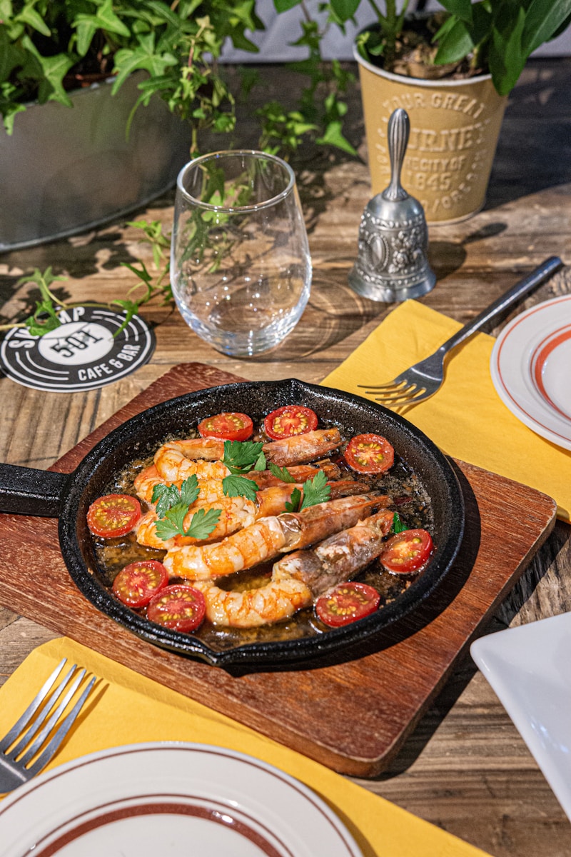 a skillet with shrimp and tomatoes on a wooden table
